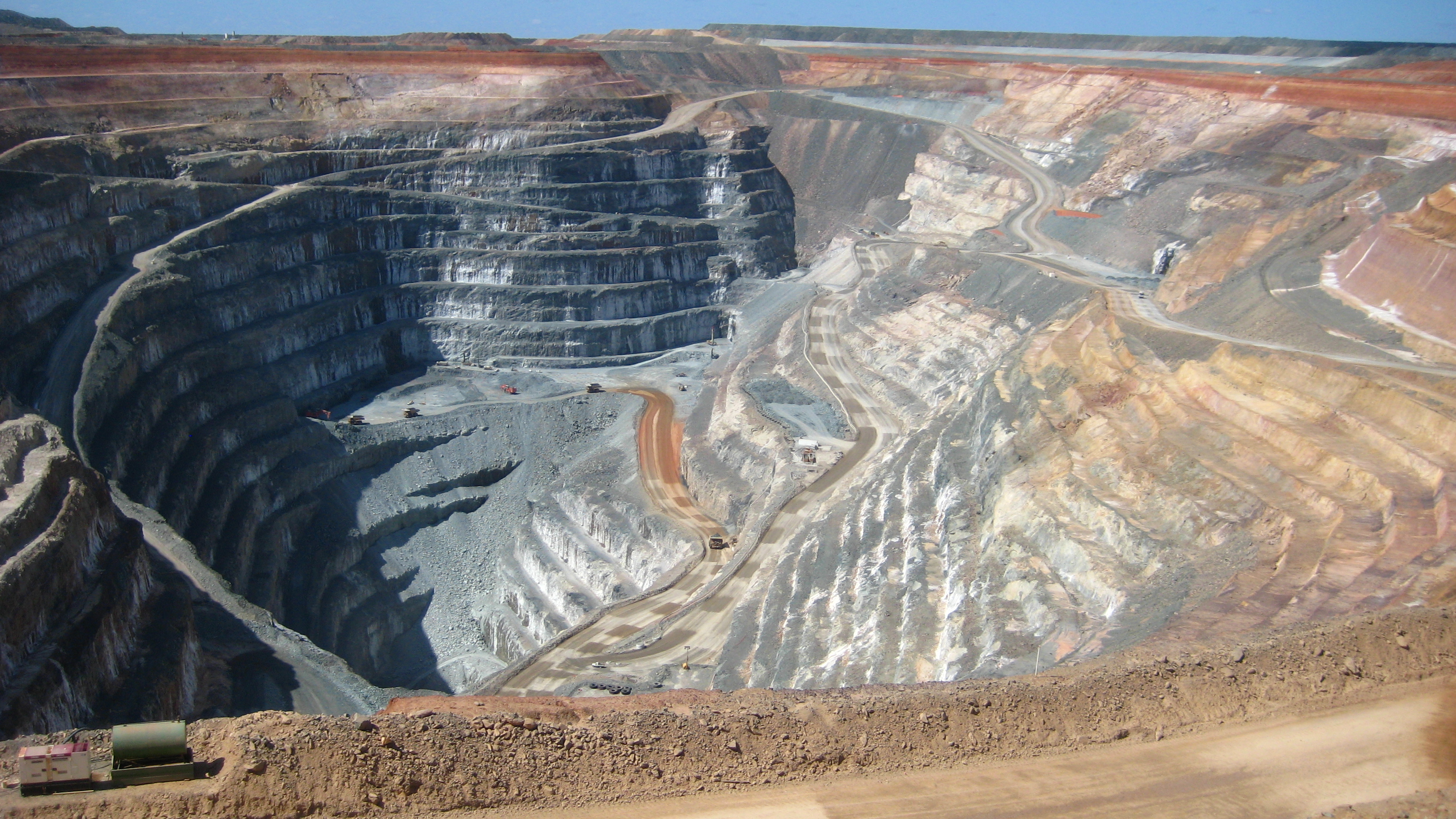 Aerial view of a large open-pit gold mine, showing terraced excavation walls and haul roads